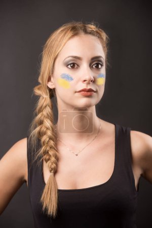 Téléchargez les photos : Portrait de belle jeune femme avec drapeau ukrainien peint sur le visage sur fond gris - en image libre de droit