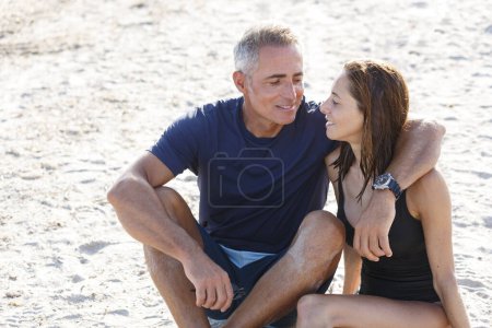 Photo for Couple in love embrace each other affectionately sitting in the sand of a beach by the sea - Royalty Free Image