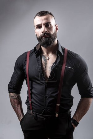 Portrait of handsome strong bearded man with tattoos on gray background