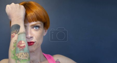Foto de Retrato de hermosa chica tatuada con el pelo rojo bob y los ojos claros, usando top de tanque rosa - Imagen libre de derechos