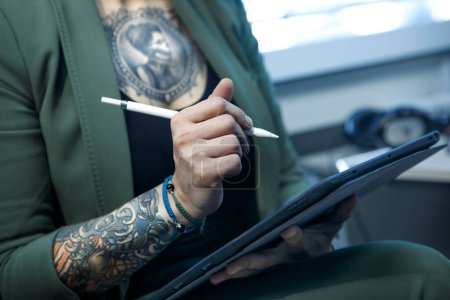 Téléchargez les photos : Vue recadrée de femme tatouée dessin sur papier avec stylo dans le bureau - en image libre de droit