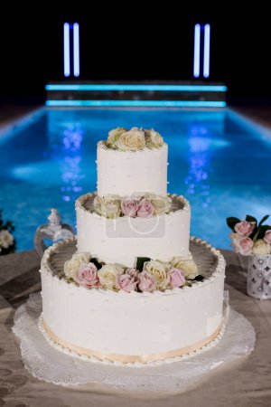 Téléchargez les photos : Gâteau de mariage blanc et rose près de la piscine la nuit - en image libre de droit