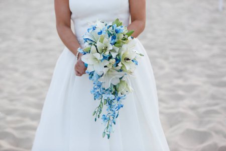 Téléchargez les photos : Bouquet de mariage entre les mains d'une mariée sur une plage de sable fin - en image libre de droit