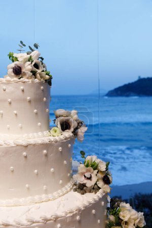 Téléchargez les photos : Gâteau de mariage avec des fleurs sur la côte de mer - en image libre de droit