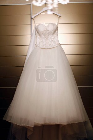 Téléchargez les photos : Belle robe de mariée accrochée au cintre dans la chambre - en image libre de droit