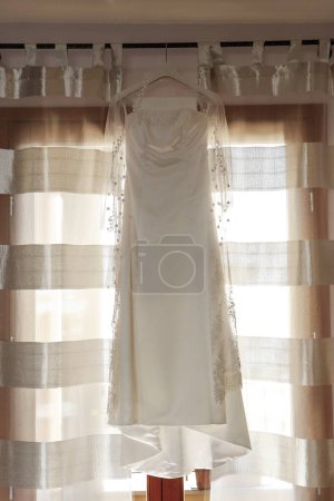 Téléchargez les photos : Robe de mariée blanche accrochée à la fenêtre d'une mariée. - en image libre de droit