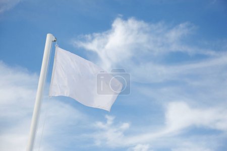Foto de Bandera blanca ondeando en el viento contra un cielo azul. de cerca. - Imagen libre de derechos