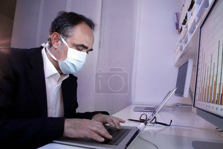 Téléchargez les photos : Homme portant un masque chirurgical travaillant avec un ordinateur portable - en image libre de droit