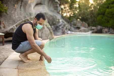 Photo for Dead man on vacation in summer outfit with hat and surgical mask relaxes in the swimming pool of a hotel - Royalty Free Image