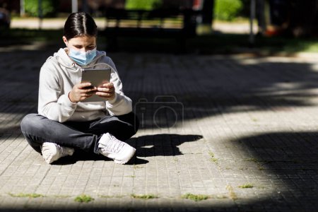 Téléchargez les photos : Femme utilisant un téléphone portable alors qu'elle était assise sur un banc en ville - en image libre de droit