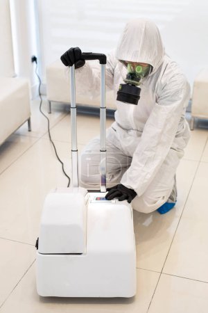 Foto de Hombre en traje protector blanco desinfectando la oficina con desinfección - Imagen libre de derechos