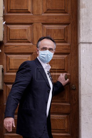 Photo for Man in jacket with protective face mask, is closing the door of the house looking worried - Royalty Free Image