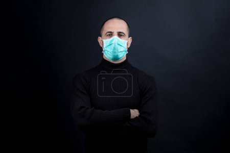 Photo for Half-length portrait of a shaved man wearing a green surgical mask, looking straight ahead, isolated on a black background - Royalty Free Image