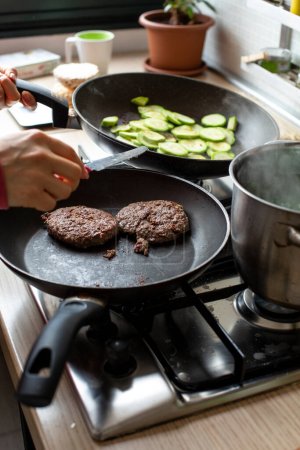 Téléchargez les photos : Hamburgers cuits dans une poêle sur une cuisinière et contrôlés par un cuisinier afin de ne pas brûler - en image libre de droit