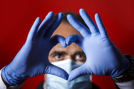Photo for Man with latex gloves forms a heart with his fingers, isolated on a red background - Royalty Free Image