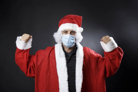 Photo for Santa Claus with surgical mask rejoices victorious, isolated on black background - Royalty Free Image