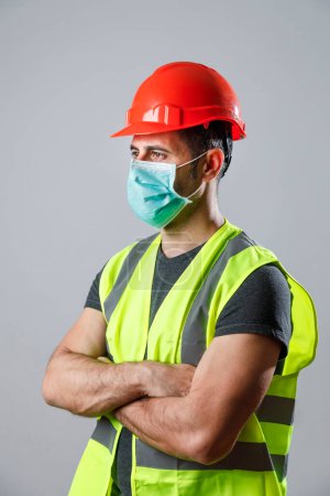 Téléchargez les photos : Travailleur avec gilet de protection jaune et masque chirurgical, isolé sur fond gris - en image libre de droit