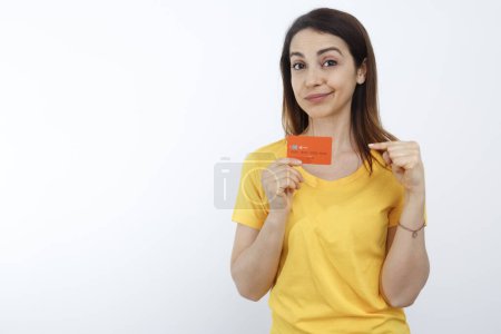 Foto de Chica morena con camisa amarilla nos mira muestra una tarjeta de crédito naranja, aislado sobre fondo blanco - Imagen libre de derechos