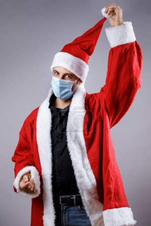 Téléchargez les photos : Père Noël avec masque chirurgical lève son chapeau, isolé sur fond neutre - en image libre de droit
