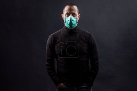 Foto de Retrato de medio cuerpo de un hombre afeitado con una máscara quirúrgica verde, mirando hacia adelante, aislado sobre un fondo negro - Imagen libre de derechos