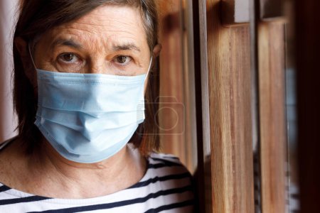 Téléchargez les photos : Femme âgée avec masque à l'intérieur de sa maison - en image libre de droit
