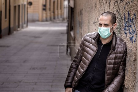 Photo for Shaven guy in dark vest wears a protective surgical mask while out and about in the city - Royalty Free Image