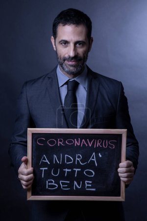 Photo for Man in suit and tie holding chalkboard that reads, "Everything will be fine." It is a wish for the coronavirus pandemic to end soon - Royalty Free Image
