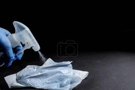 Photo for Hand with protective glove sprays the spray with a nebulizer over a cloth, isolated on a black background - Royalty Free Image