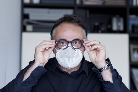 Photo for Portrait of dark haired man with face mask and eyeglasses isolated in home setting - Royalty Free Image
