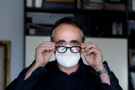 Photo for Portrait of dark haired man with face mask and eyeglasses isolated in home setting - Royalty Free Image