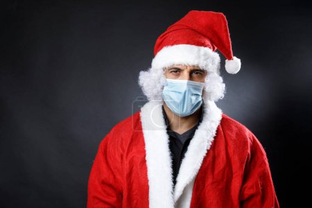 Téléchargez les photos : Père Noël avec masque chirurgical semble grave et inquiet, isolé sur fond noir - en image libre de droit