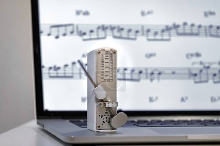 Photo for Musical metronome and in the background sheet music on a computer - Royalty Free Image