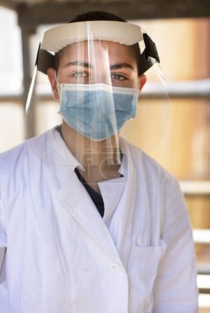 Photo for Young researcher with white coat, protective shield, face mask and protective helmet in an industrial context - Royalty Free Image