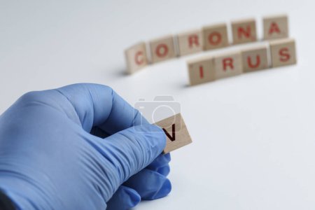 Photo for Written "virus crown" with wooden letters while a gloved hand holds the letter "V", isolated on a white background - Royalty Free Image