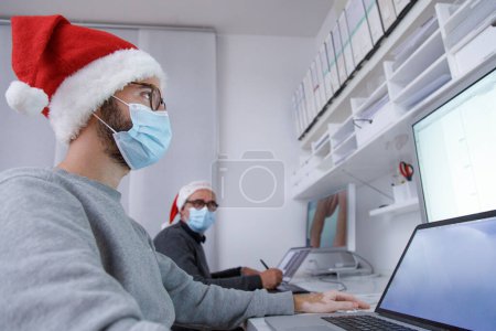 Photo for Men in a medical masks working in the office with a laptops, Christmas concept, new year, pandemic coronavirus - Royalty Free Image