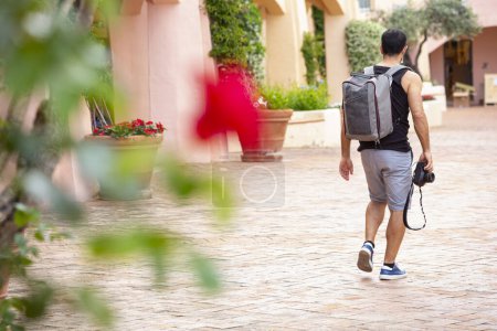 Foto de Hombre de vacaciones en traje de verano pasea por un pueblo con mochila y cámara - Imagen libre de derechos