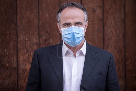 Photo for Man dressed in suit with protective face mask isolated on wooden background - Royalty Free Image