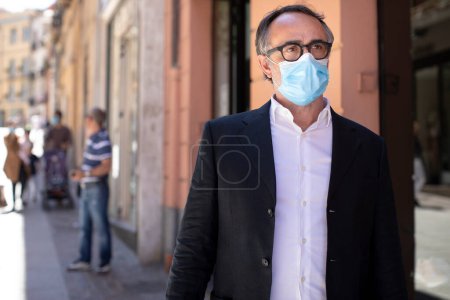 Foto de Hombre con chaqueta y mascarilla quirúrgica está parado en una calle del centro de la ciudad - Imagen libre de derechos