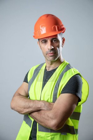 Photo for Portrait dark-haired worker with helmet and yellow vest, isolated on light background - Royalty Free Image