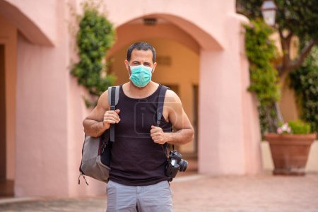 Foto de Hombre moreno con camiseta y mochila de vacaciones con mascarilla protectora - Imagen libre de derechos
