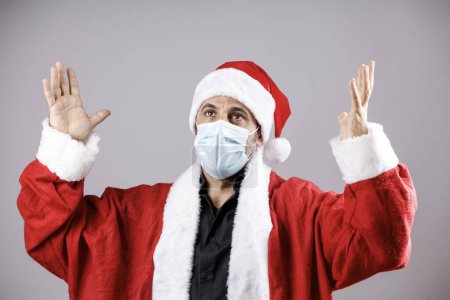 Téléchargez les photos : Père Noël avec masque chirurgical lève les bras vers le ciel dans le désespoir, isolé sur fond blanc - en image libre de droit