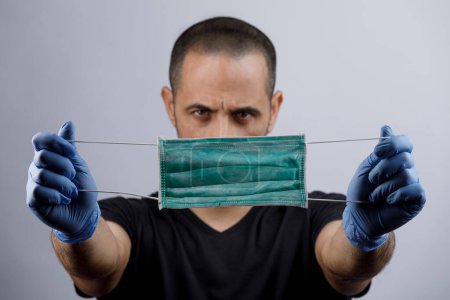 Photo for Man with and latex gloves holds in his hand a green protective face mask, isolated on light background - Royalty Free Image