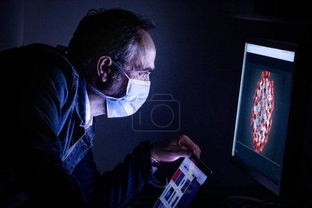 Photo for Man with a mask and a computer in his workplace at night - Royalty Free Image