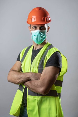 Foto de Trabajador con chaleco protector amarillo y máscara quirúrgica, aislado sobre fondo gris - Imagen libre de derechos