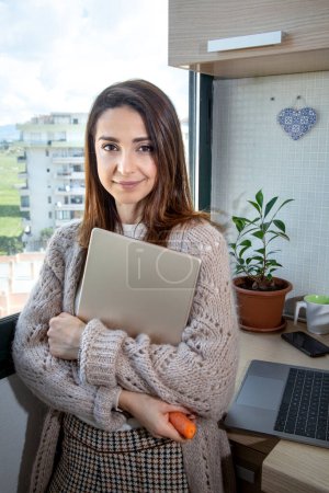 Photo for Brunette girl with laptop in hand smiles near the window - Royalty Free Image