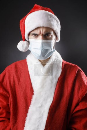 Téléchargez les photos : Père Noël avec masque chirurgical se réjouit victorieux, isolé sur fond noir - en image libre de droit