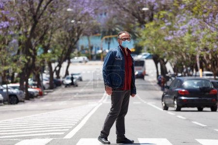 Téléchargez les photos : Homme brun avec masque facial et robe décontractée, traverse la rue sur les passages piétons d'une rue animée dans le centre - en image libre de droit