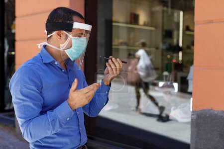 Foto de Hombre con máscara vestida casual se protege en la ciudad mientras habla en un teléfono celular - Imagen libre de derechos