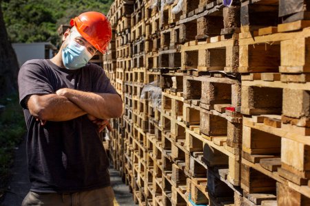 Photo for Worker with protective helmet immersed in stacked pallets - Royalty Free Image