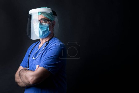 Foto de Médico de capa azul con protecciones y protector facial aislado sobre fondo negro - Imagen libre de derechos